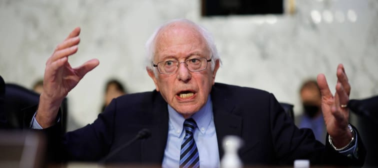 Bernie Sanders speaks in a Congressional hearing with his hands up in the air and an exasperated look on his face.